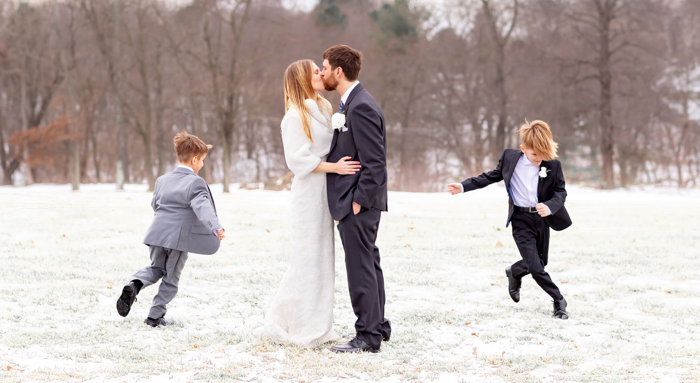 Wedding couple kissing in the snow with two boys playing